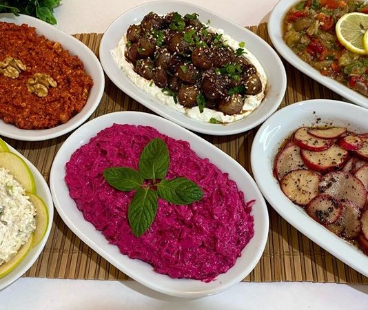 Mezeler, Türk ve Akdeniz mutfaklarının en özel ve zengin yanlarından biridir. Hem ana yemeklerin yanında sunulan hem de tek başına sofraları zenginleştiren bu küçük lezzetler, misafir ağırlamanın da baş tacıdır. Mezeler, farklı malzemelerden oluşan çeşitleriyle her damak tadına hitap ederken, aynı zamanda sofraların renkli ve şık görünmesini sağlar. Pratik hazırlanabilir olmaları ve geniş yelpazede sunulmaları sebebiyle hem evde hem de restoranlarda sıkça tercih edilir. Konulu bir haber görseli.