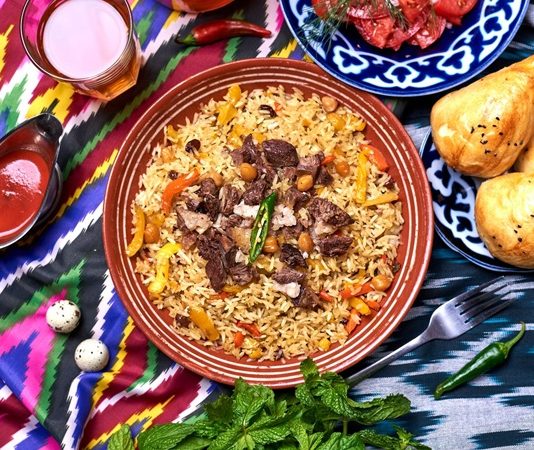 Özbekistan mutfağı, Orta Asya’nın bereketli topraklarında, tarih boyunca farklı kültürlerin etkisiyle şekillenmiş zengin bir gastronomi mirasına sahiptir. İpek Yolu’nun kesişim noktalarından biri olan Özbekistan, hem Doğu hem de Batı mutfak geleneklerini harmanlamış, yemek kültürünü çeşitlendirmiştir. Et ve tahıllar, mutfağın temelini oluştururken; baharatlar ve taze sebzeler, yemeklere özgün tat ve aroma kazandırır. Konulu bir haber görseli.