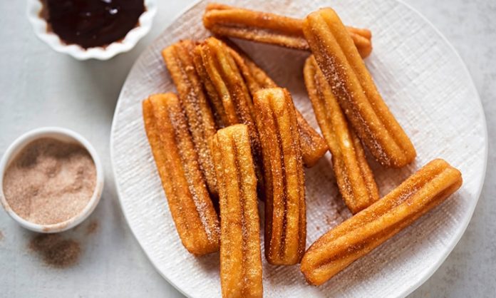 Churros Sokak Lezzetinden Sofralara Uzanan Tatlı Hikayesi Churros, İspanya kökenli, kızartılarak hazırlanan tatlı hamur çubuklarıdır. 19. yüzyılda İspanya’da ortaya çıkan bu lezzet, kısa sürede Latin Amerika ve dünyanın farklı bölgelerine yayılmıştır. Geleneksel olarak kahvaltıda veya akşamüstü çay saatlerinde tüketilen churros, sıcak çikolata veya karamel sosla birlikte sunulur. Konulu bir haber görseli.