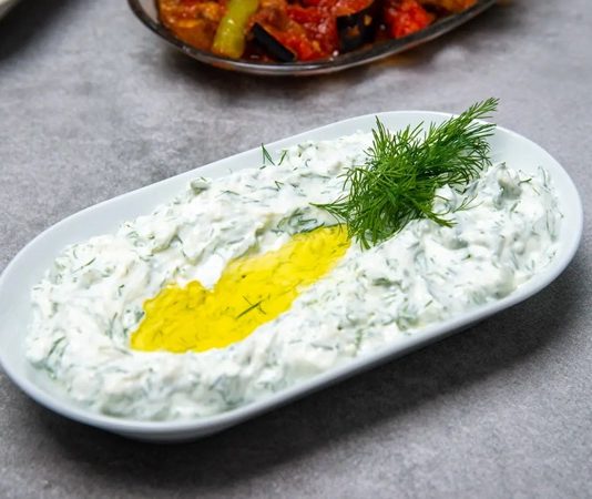 Haydari, özellikle kahvaltı sofralarının ve mezelerin vazgeçilmez tatlarından biridir. Yoğurt bazlı bu lezzetli meze, hem hafif hem de besleyici olmasıyla öne çıkar. Haydari, yüksek protein içeriği sayesinde kas ve kemik sağlığını desteklerken, probiyotik özelliği ile sindirim sistemine katkıda bulunur. İçerdiği sarımsak ve dereotu gibi doğal malzemeler, lezzetin yanı sıra sağlık açısından da avantaj sağlar. Konulu bir haber görseli.