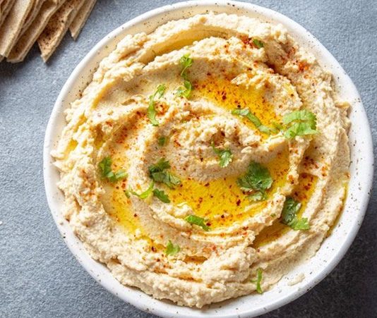 Humus, Orta Doğu mutfağının en bilinen ve sevilen mezelerinden biridir. Başlıca malzemeleri nohut, tahin, limon suyu, sarımsak ve zeytinyağı olan bu özel tarif, yüzyıllardır sofralarda yerini almaktadır. Tarihi çok eski dönemlere dayanan humus, özellikle Lübnan, Suriye, Filistin ve Türkiye gibi bölgelerde yaygın olarak tüketilir. Bugün ise dünya genelinde sağlıklı bir atıştırmalık ya da ana yemek yanında tamamlayıcı olarak tercih edilmektedir. Konulu bir haber görseli.