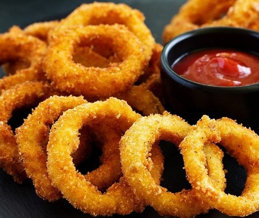 Soğan halkası, fast food kültürünün en sevilen atıştırmalıklarından biri olarak öne çıkıyor. Tarihi 20. yüzyılın ortalarına dayanan bu lezzet, özellikle Amerika’da popülerlik kazanmış ve kısa sürede dünya mutfaklarına yayılmıştır. Patates kızartmaları ve burgerlerin yanında ikincil lezzet olarak sunulan soğan halkaları, hem çıtır dokusu hem de tatlımsı soğan aroması ile dikkat çekiyor. Konulu bir haber görseli.