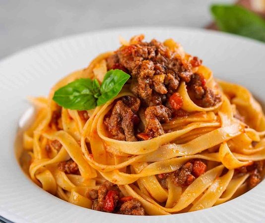 Tagliatelle, İtalyan mutfağının en tanınmış makarna çeşitlerinden biri olarak bilinir. Genellikle geniş ve uzun şeritler halinde hazırlanır. Bu makarna türü, özellikle Bolognese sosu ile eşsiz bir uyum yakalar ve İtalya’nın Emilia-Romagna bölgesinde köklü bir geçmişe sahiptir. Konulu bir haber görseli.