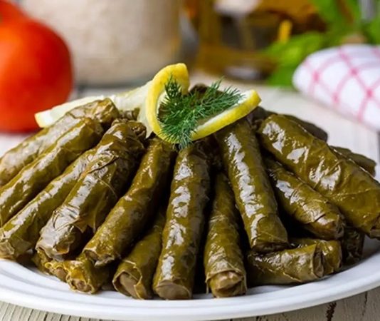 Zeytinyağlı Yaprak Sarma: Sofraların Vazgeçilmez Lezzeti Zeytinyağlı yaprak sarma, Türk mutfağının en sevilen geleneksel lezzetlerinden biridir. Özellikle meze olarak sofralarda sıkça yer alır ve hem hafif hem de besleyici bir alternatif sunar. Yaprak sarması, sadece Türkiye’de değil, Orta Doğu ve Balkan mutfaklarında da farklı yorumlarla hazırlanır. Konulu bir haber görseli.