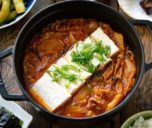 Kimchi Jjigae Kore Mutfağının Baharatlı ve Sağlıklı Çorbası Globalleşiyor Güney Kore mutfağının en ikonik çorbalarından biri olan Kimchi Jjigae, son yıllarda dünya genelinde hem restoran menülerinde hem de ev yapımı tariflerde popülerliğini artırıyor. Özellikle fermente lahana, baharatlı biber ve dengeli et suyu ile hazırlanan bu çorba, hem doyurucu hem de sağlık açısından zengin bir yemek olarak öne çıkıyor. Türkiye’de de gastronomi meraklılarının ilgisini çeken Kimchi Jjigae, Kore mutfağının globalleşmesinde önemli bir rol oynuyor. Lezzeti ve besleyici özellikleri sayesinde çorba severler için hem geleneksel hem de modern alternatifler sunuyor. Konulu bir haber görseli.
