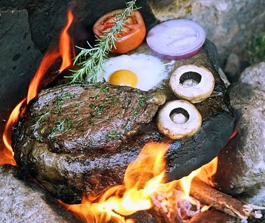 Yemek pişirme teknikleri, insanlık tarihinin en eski kültürel pratiklerinden biri olarak kabul edilir. Bu teknikler arasında yer alan Isıtılmış Taş Üzerinde Pişirme, doğayla doğrudan temas kuran, ilkel ama bir o kadar da etkili bir yöntem olarak öne çıkar. Ateşle ısıtılan taşların üzerinde ya da taşların yardımıyla yapılan bu pişirme biçimi, hem tarihsel hem de kültürel açıdan güçlü anlamlar taşır. Günümüzde gastronomi dünyasında yeniden ilgi gören bu yöntem, geçmişle bugünü aynı sofrada buluşturur. Konulu bir haber görseli.