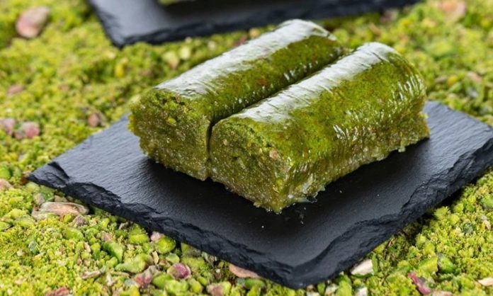 Fıstıklı Sarma Tatlısının Osmanlı’dan Günümüze Uzanan Lezzet Yolculuğ Fıstıklı sarma, Türk tatlı kültürünün hem tarihsel hem damak zevki açısından en özel lezzetlerinden biri olarak biliniyor. Osmanlı saray mutfağından günümüze taşınan zengin mirasın bir parçası olan bu tatlı, özellikle özel günlerde, bayram sofralarında ve davet masalarında sıklıkla tercih ediliyor. Bu nedenle sadece gastronomik bir tatlı olmakla kalmayan fıstıklı sarma, kültürel bir simge haline gelmiş durumda. Şerbetli tatlılar arasında kendine özgü yapısıyla farklı bir yer edinen bu lezzet, hem yapımı hem sunumu hem de ustalığıyla dikkat çekiyor. Konulu bir haber görseli.