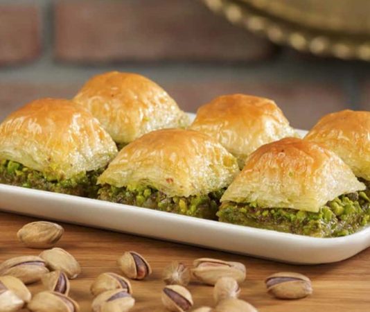 Türkiye’nin en özel tatlılarından biri olan baklava, yüzyıllar boyunca hem coğrafyalara hem de kültürlere yayılan zengin bir mirasa sahip. Orta Asya’dan Anadolu’ya uzanan serüveniyle bugün dünyanın dört bir yanında tanınan bir lezzet hâline gelen baklava, Osmanlı mutfağından itibaren saray sofralarının vazgeçilmez tatlısı olarak kayıt altına alınmıştır. Bu süreçte tatlının yapım teknikleri geliştirilmiş, farklı yörelerde kendine has çeşitleri ortaya çıkmıştır. Gaziantep baklavası, bu tarihsel yolculukta en çok bilinen ve coğrafi işaret tesciline sahip örneklerden biridir. Konulu bir haber görseli.