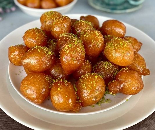 Lokma Tatlısı Gelenekten Günümüze Ulaşan Benzersiz Bir Lezzet Türkiye’nin en sevilen tatlılarından biri olan lokma tatlısı, geçmişten bugüne gelen bir kültür mirasının lezzete dönüşmüş hâli olarak dikkat çekiyor. Osmanlı mutfağında önemli bir yere sahip olan lokma, günümüzde sokak lezzeti olarak yaygınlaşmış ve neredeyse her şehirde farklı hazırlanış şekilleriyle sunulmaya başlamıştır. Özellikle son yıllarda özel günlerde, hayır etkinliklerinde ve sosyal organizasyonlarda daha sık karşımıza çıkan lokma tatlısı, geleneksel tariften modern tariflere kadar geniş bir çeşitlilik sunmaya devam ediyor. Bu nedenle hem nostalji taşıyan hem de yeniliğe açık bir tatlı olarak gastronomideki yerini pekiştiriyor. Konulu bir haber görseli.